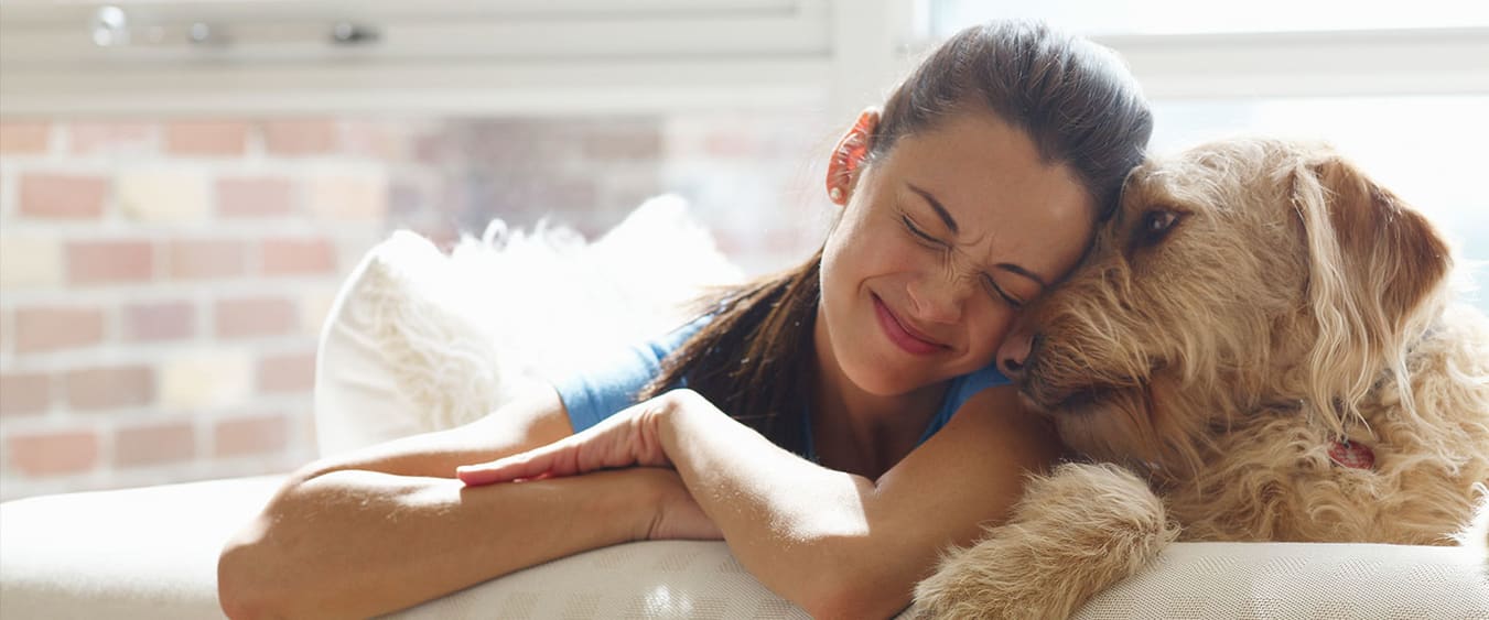 Femme souriante les yeux fermés, câlinant un chien sur le canapé